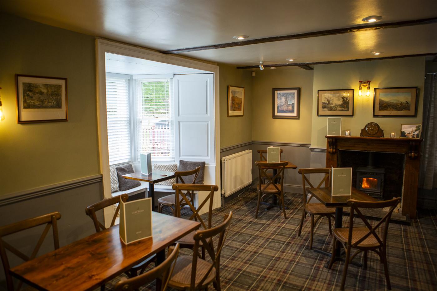 Dining room with wooden tables, tartan carpet and a lit fireplace