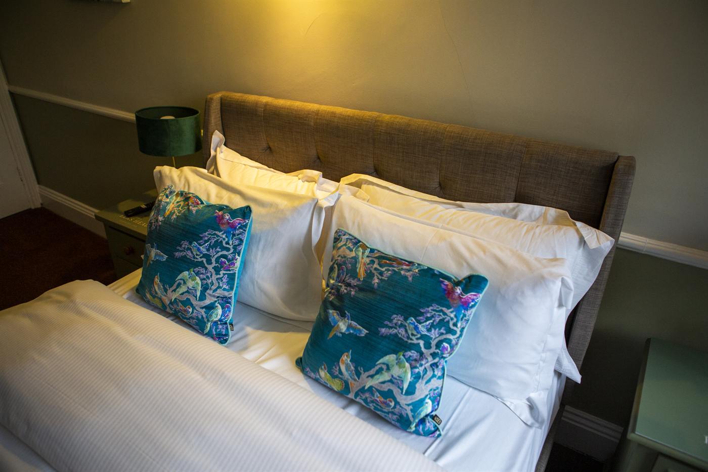 A double bed with crisp white linen and teal cushions