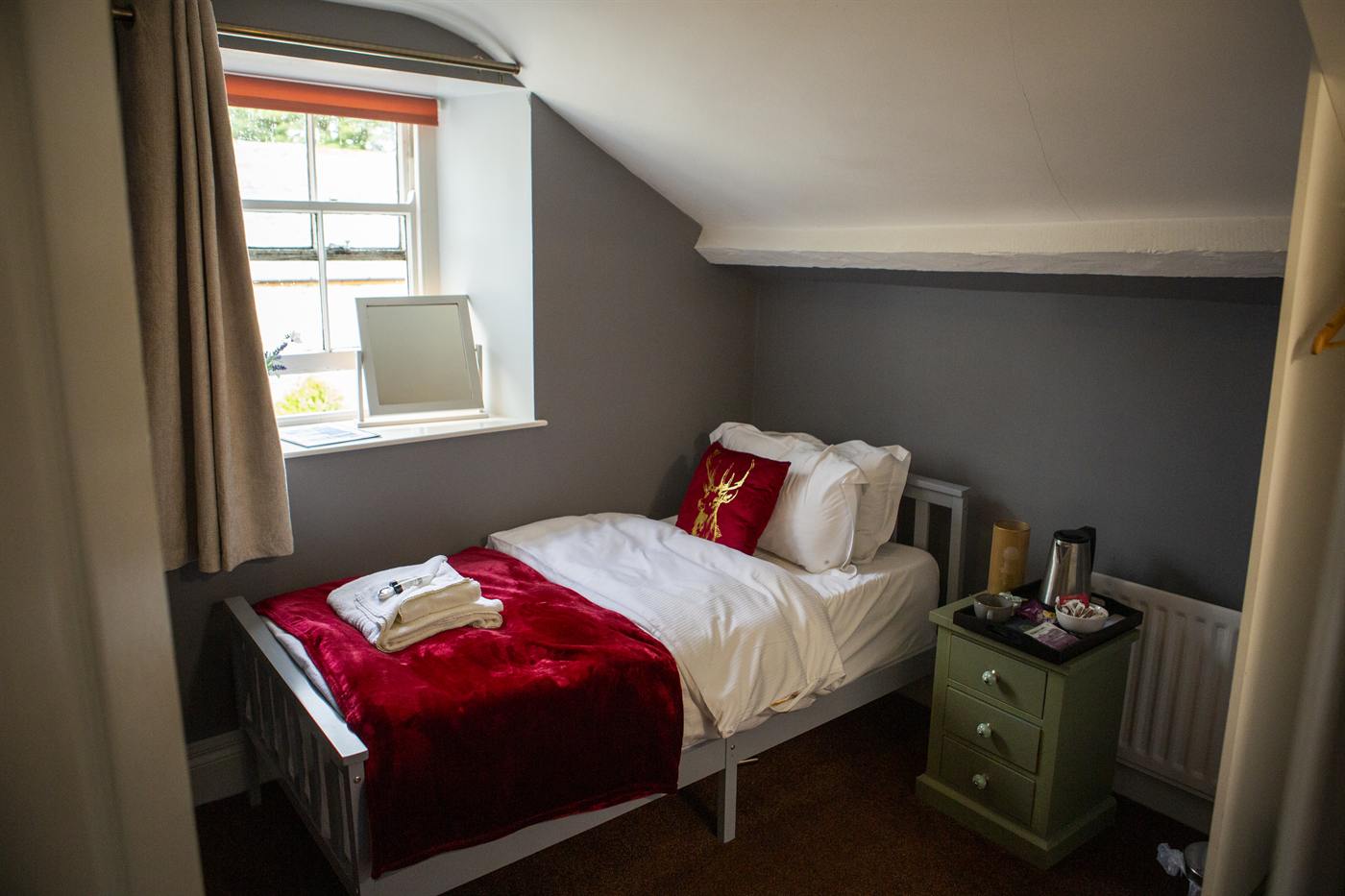 A cosy single bedroom with a red throw, Elks Head cushion and a window seat view