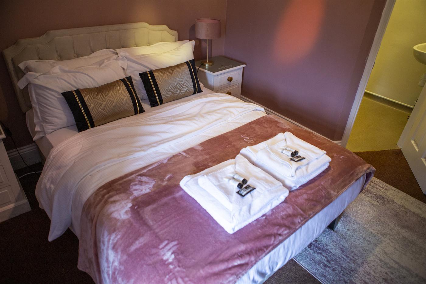 A double bed with a pink velvet runner and fresh towels
