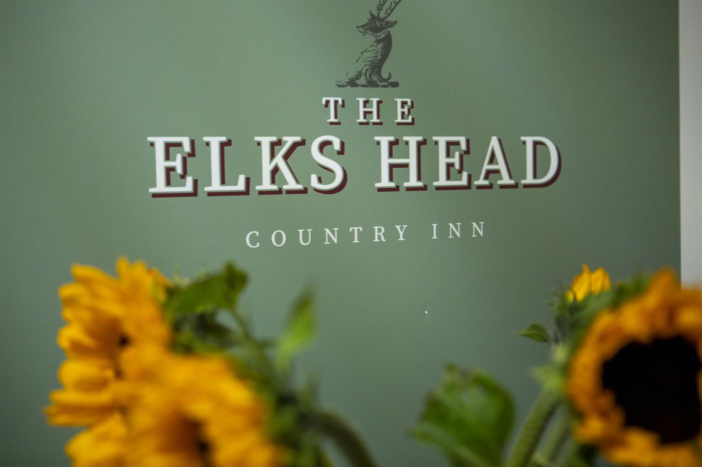 The Elks Head Country Inn logo on the wall behind a vase of sunflowers