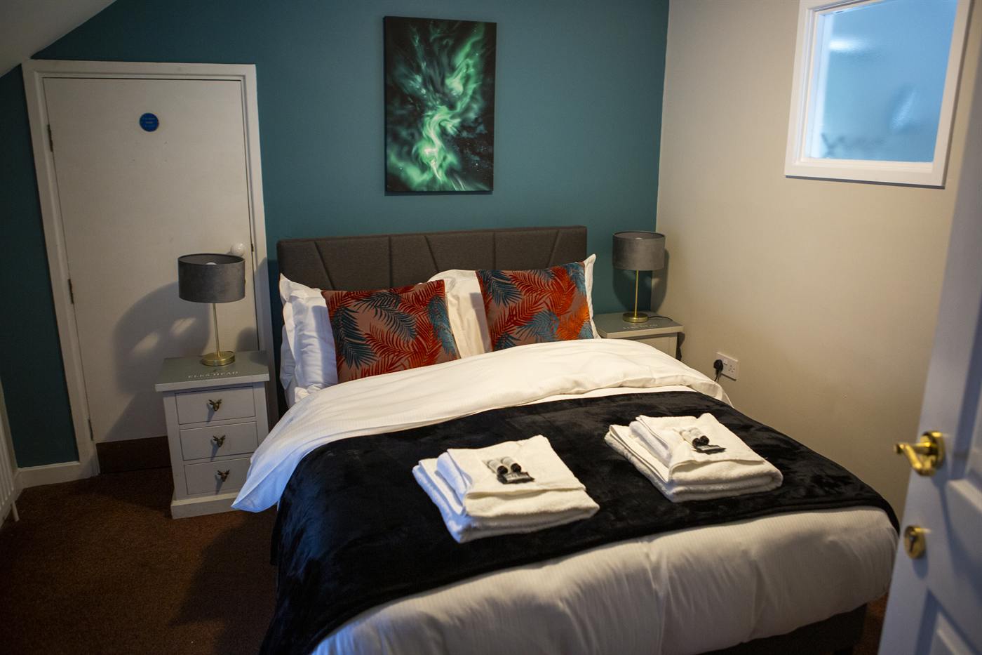 A double bedroom with teal walls, colourful cushions and fresh towels