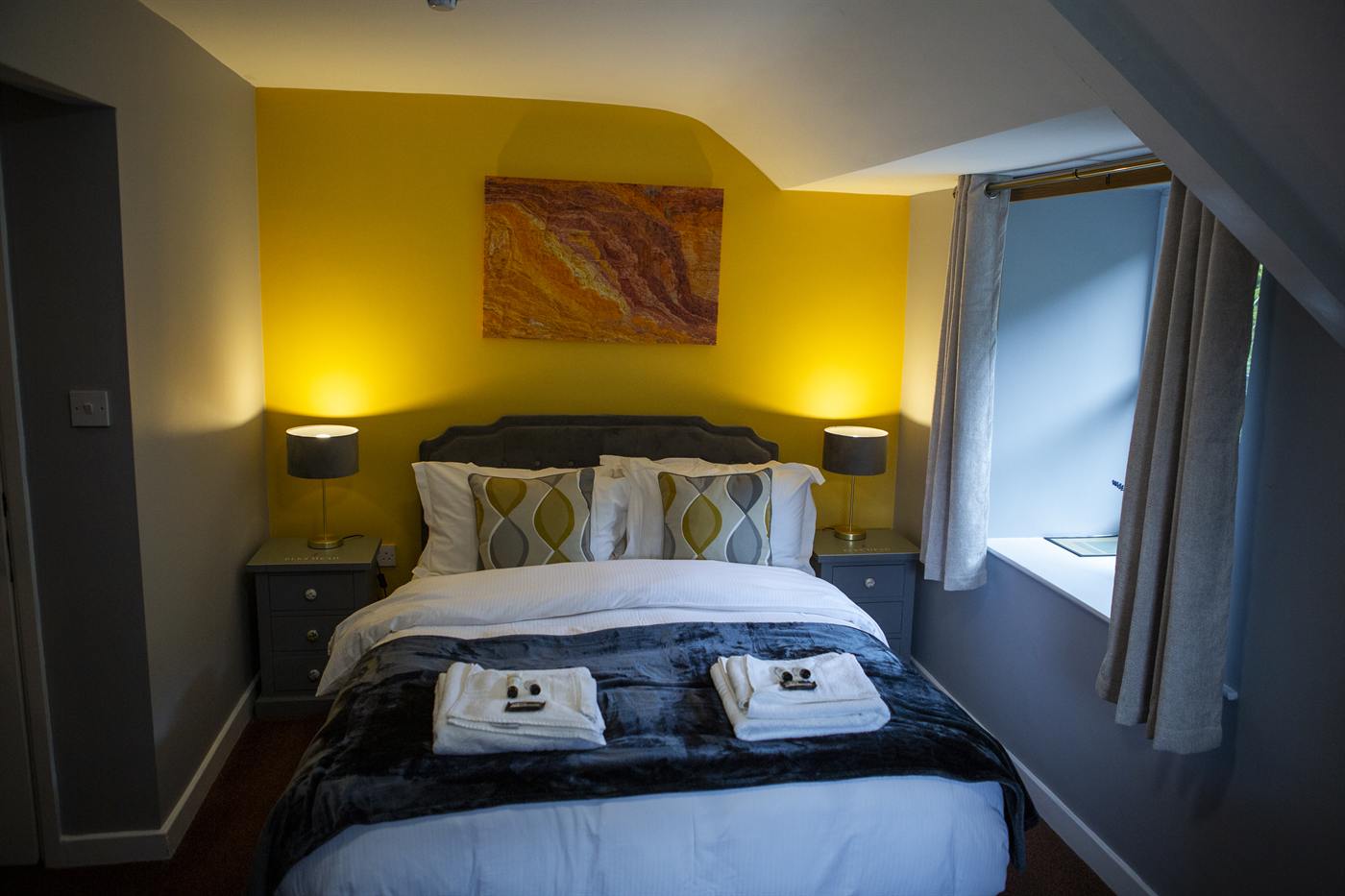 A double bedroom with warm yellow walls and bedside lamps